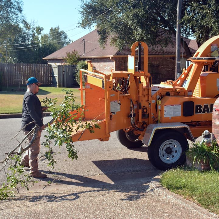 Crew feeding storm brush into a wood chipper on a residential street — cleanup included